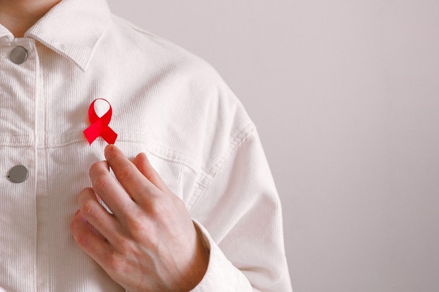 ŽIV raudonas kaspinas, kurį dėvi vyras baltais marškiniais